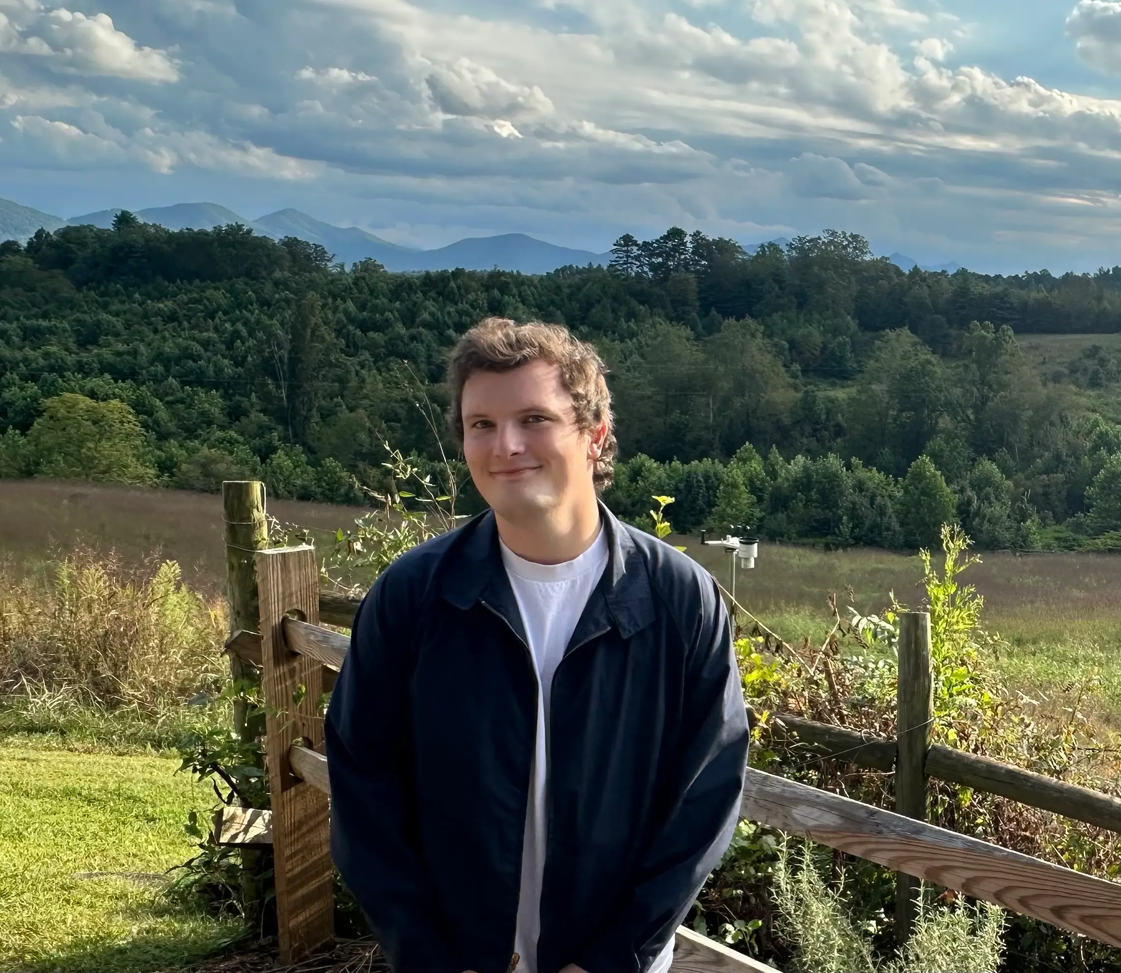 A UNC medical student and scholarship recipient stands outdoors with a mountain landscape in the background, representing a commitment to improving healthcare access in rural communities.