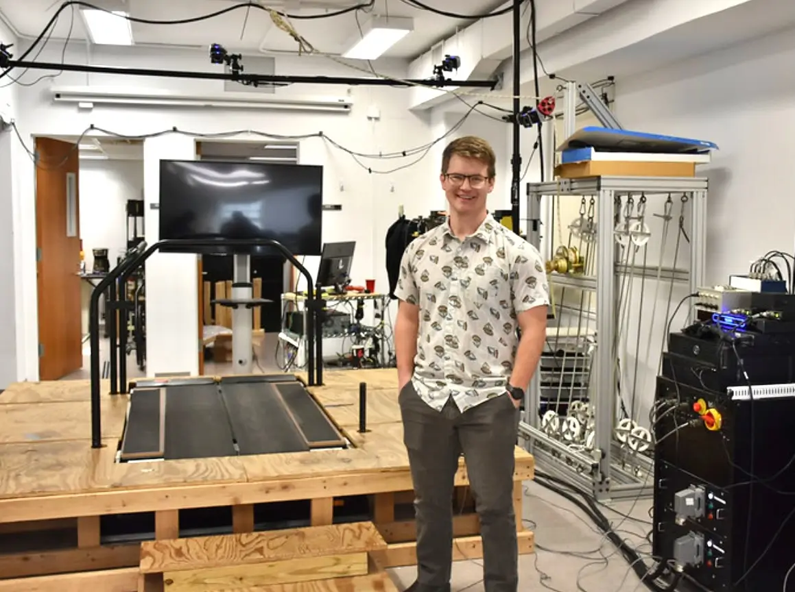 A UNC researcher stands inside a biomechanics laboratory featuring a gait analysis treadmill and motion capture equipment used to study mobility and Parkinson’s disease.