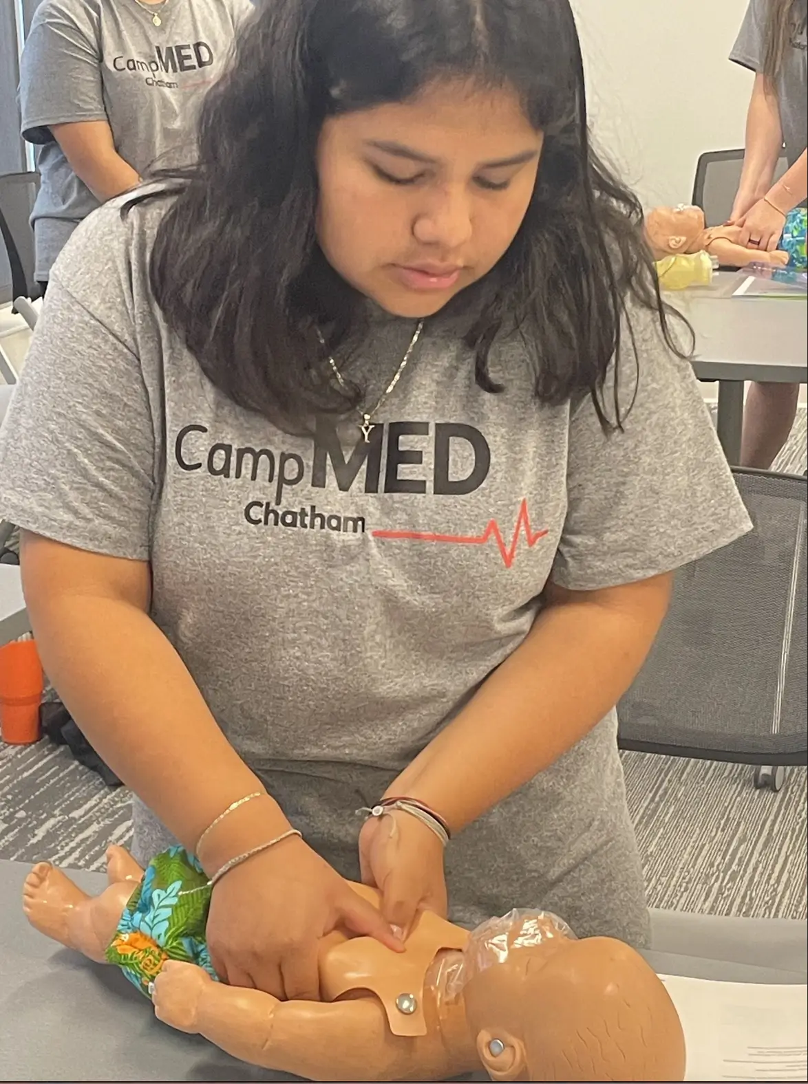 CampMED student practices infant CPR chest compressions on a pediatric training mannequin during a hands-on emergency response workshop made possible by UNC Hospital donations