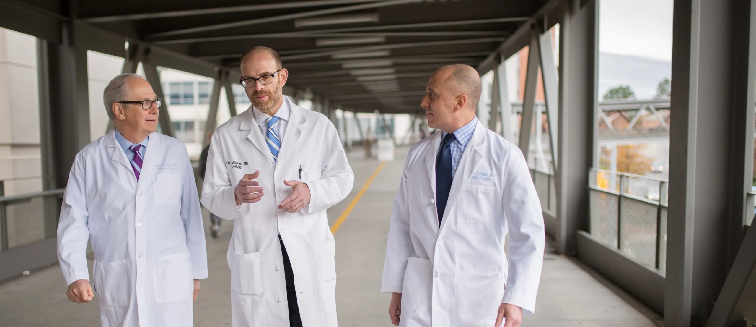 Three UNC physicians in white coats walk together while discussing cardiovascular research findings.