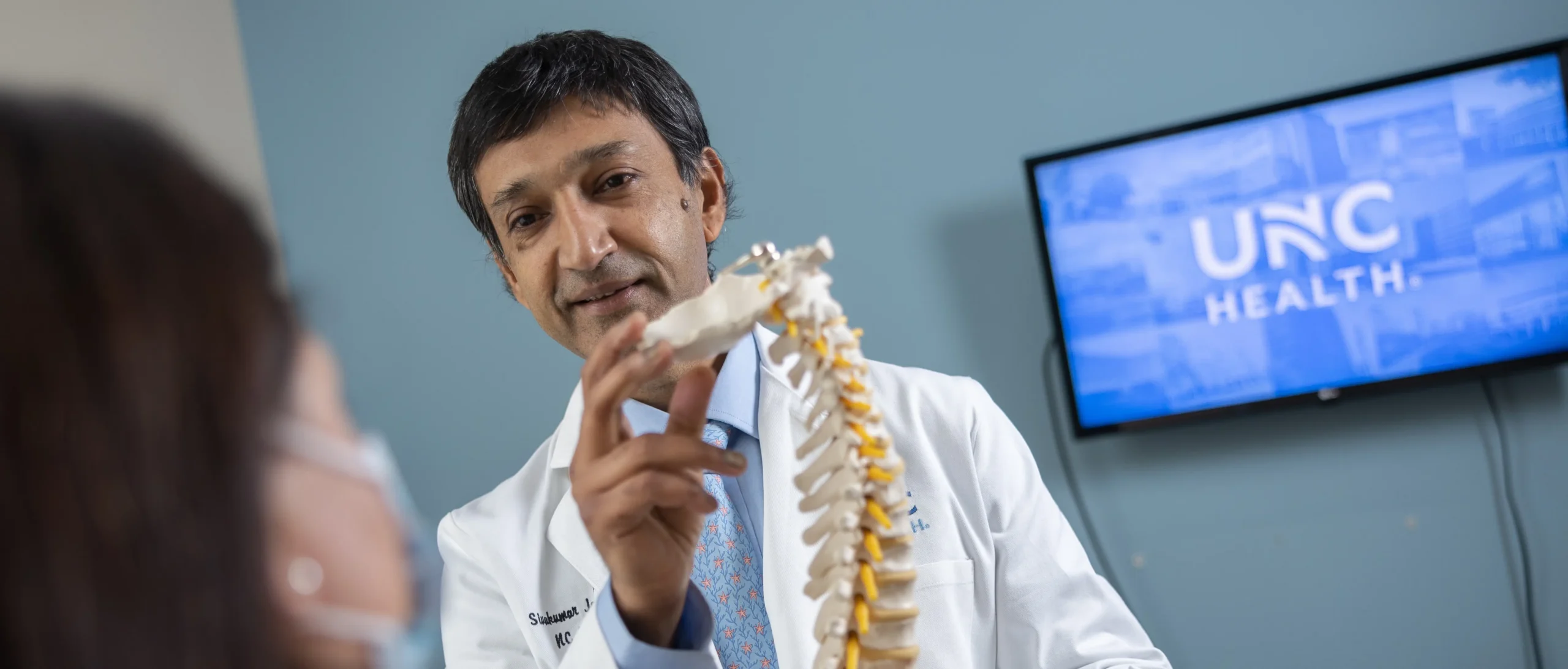 UNC Neuroscience Center physician explains the latest neuroscience research to a patient using a spinal model during a medical consultation.