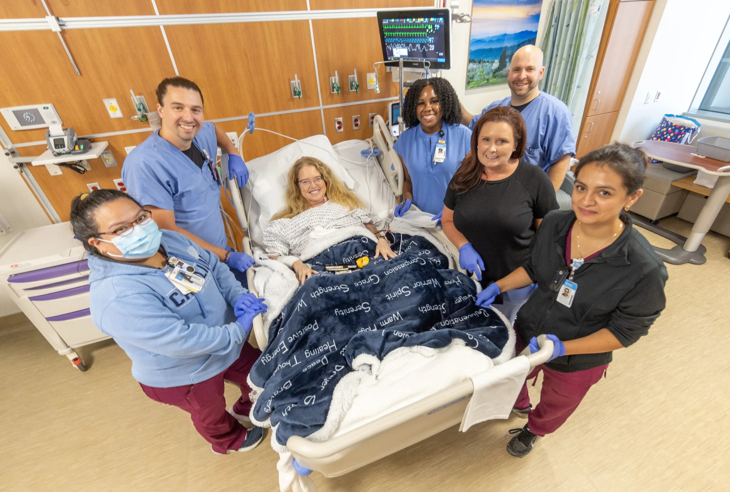 Patient resting in a hospital bed surrounded by a team of healthcare staff in a hospital room, highlighting the potential of employee giving at UNC