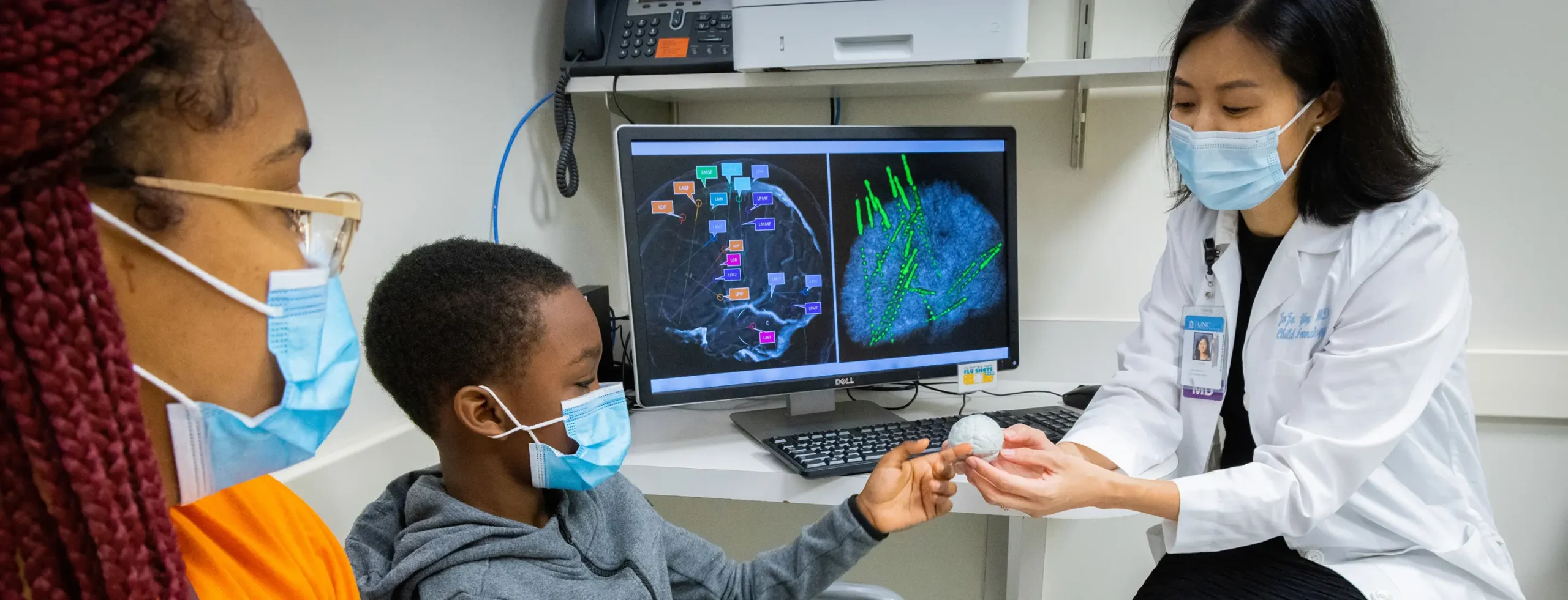 Pediatric neurologist showing a brain model to a child and caregiver during a consultation in a behavioral health research clinic
