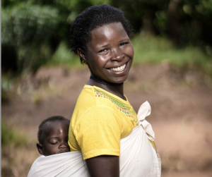 A smiling mother carrying her child in a traditional wrap.