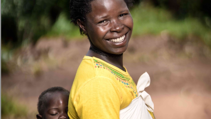 A smiling mother carrying her child in a traditional wrap.