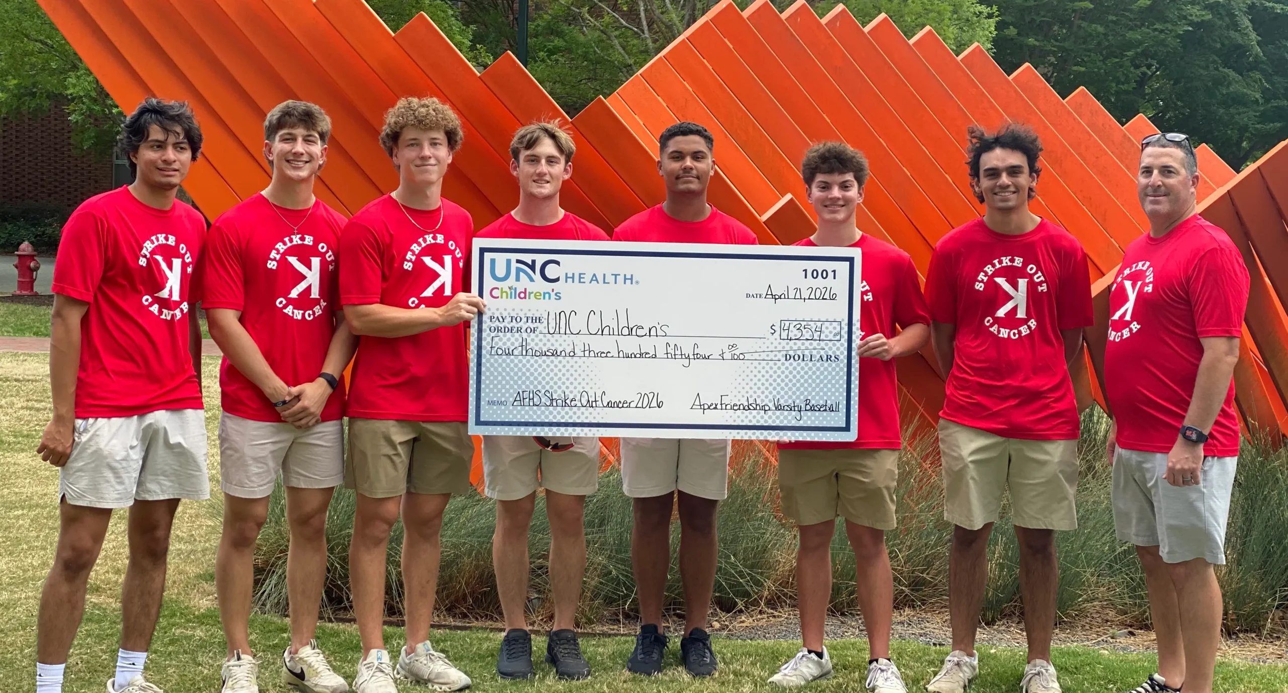 Group wearing Strike Out Cancer shirts presents a large donation check to UNC Children’s Hospital in support of cancer care.