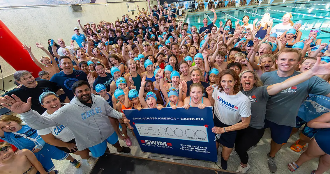 Large group of swimmers, families, and supporters gathered at an indoor pool for a Swim Across America fundraising event.