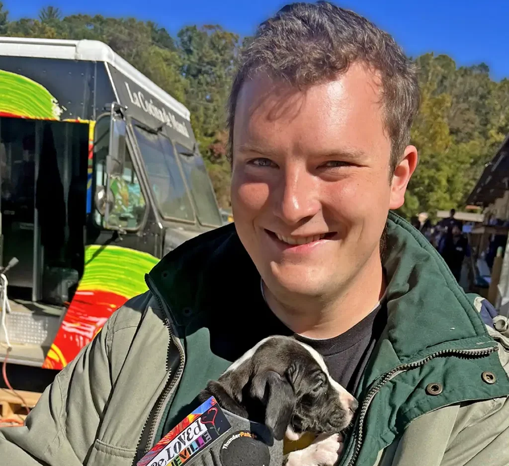 News story featuring a UNC School of Medicine scholarship recipient smiling while holding an adoptable puppy at an outdoor community outreach event, highlighting the kinds of treatment programs that become possible through healthcare philanthropy