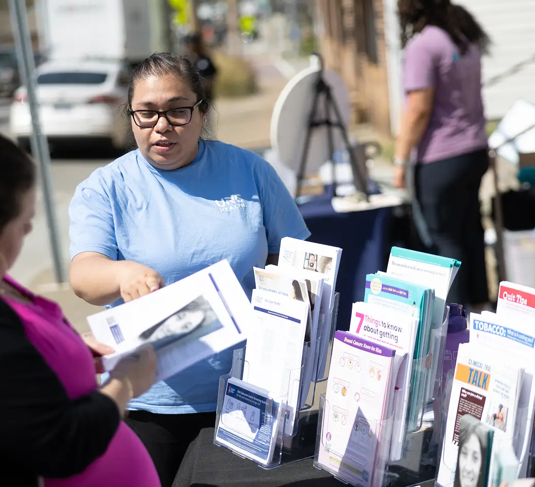 Healthcare outreach representative providing educational resources and wellness information to a community member at a public health event sponsored by donor fundraising